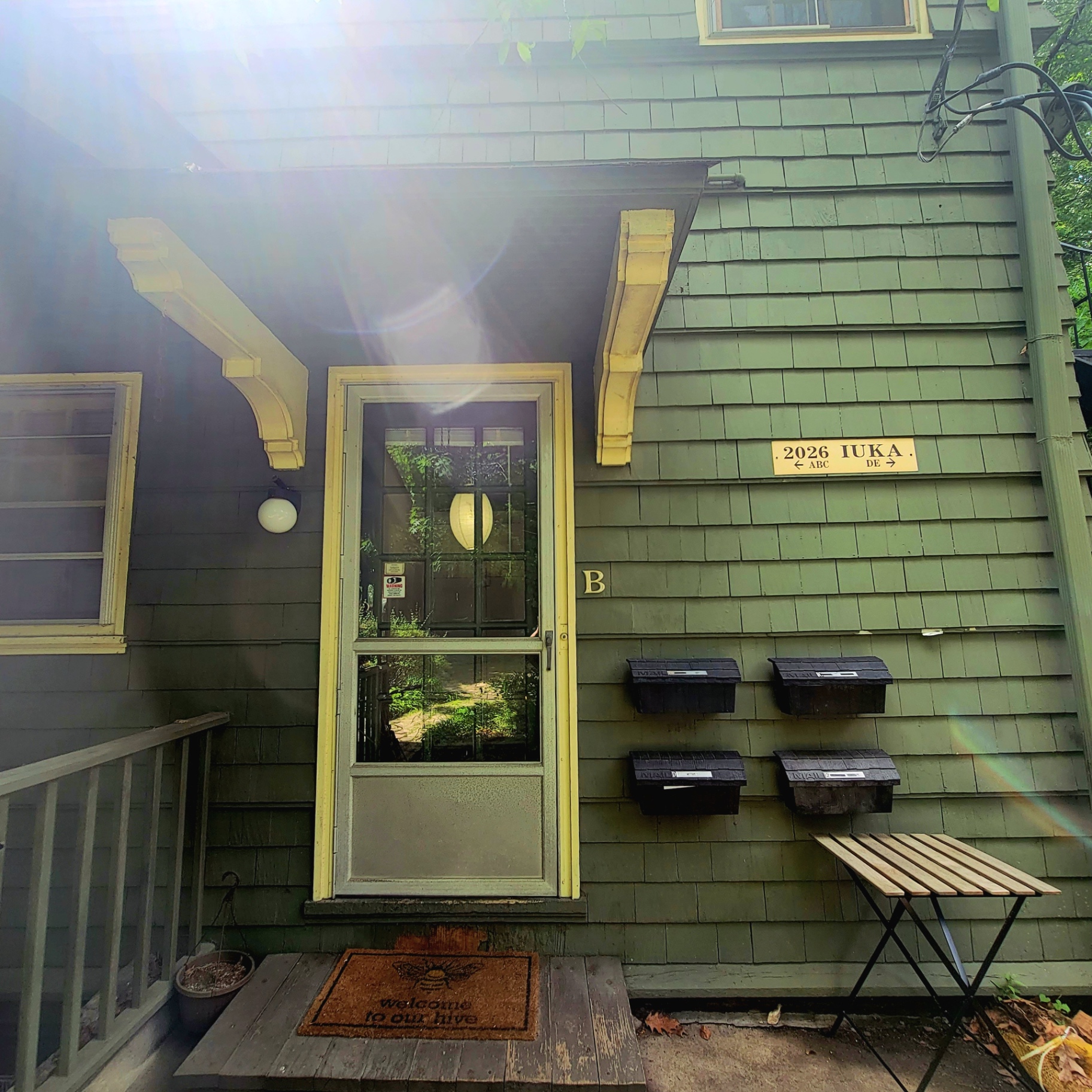 2026 Iuka Ave B private entry with yellow-trimmed door and green shingle siding