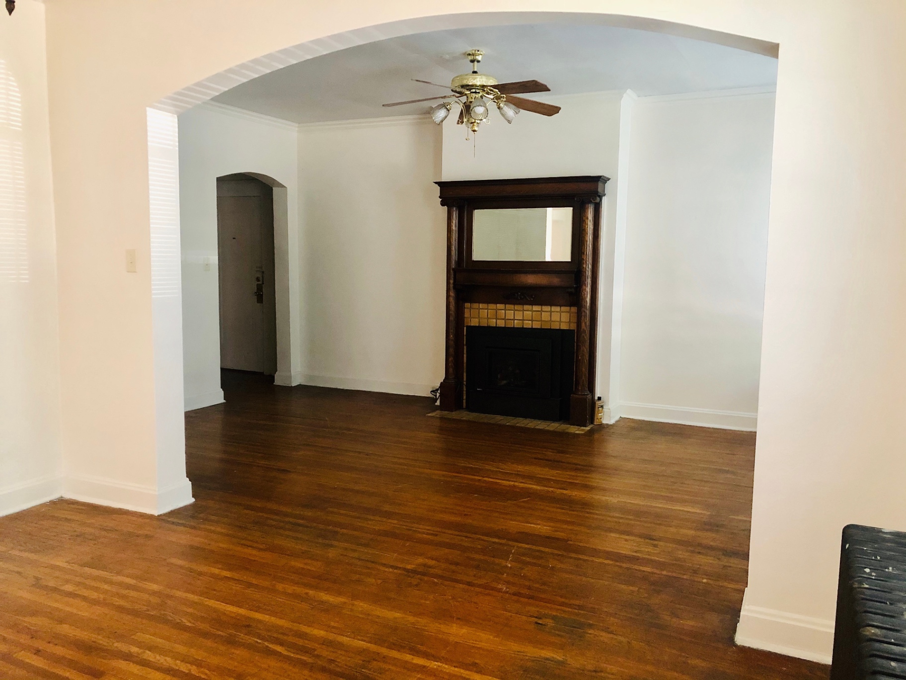 Unit G living room with dark wood-mantel fireplace, arched entryway, and hardwood floors