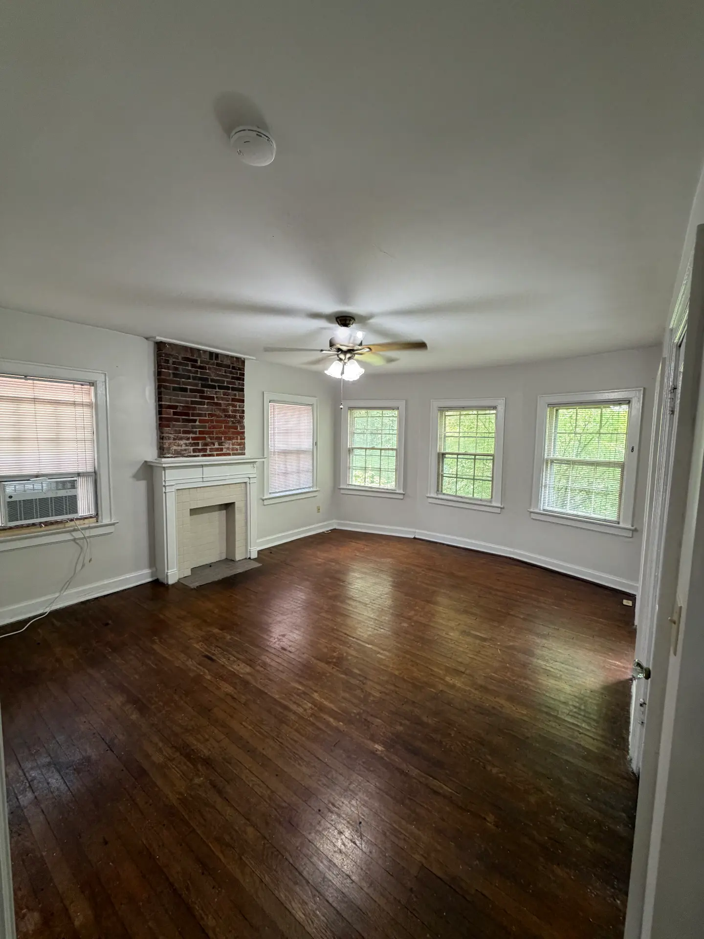 2048 Iuka Ave. D living room with exposed brick chimney, white tile fireplace, ceiling fan, and bay of windows over hardwood floors
