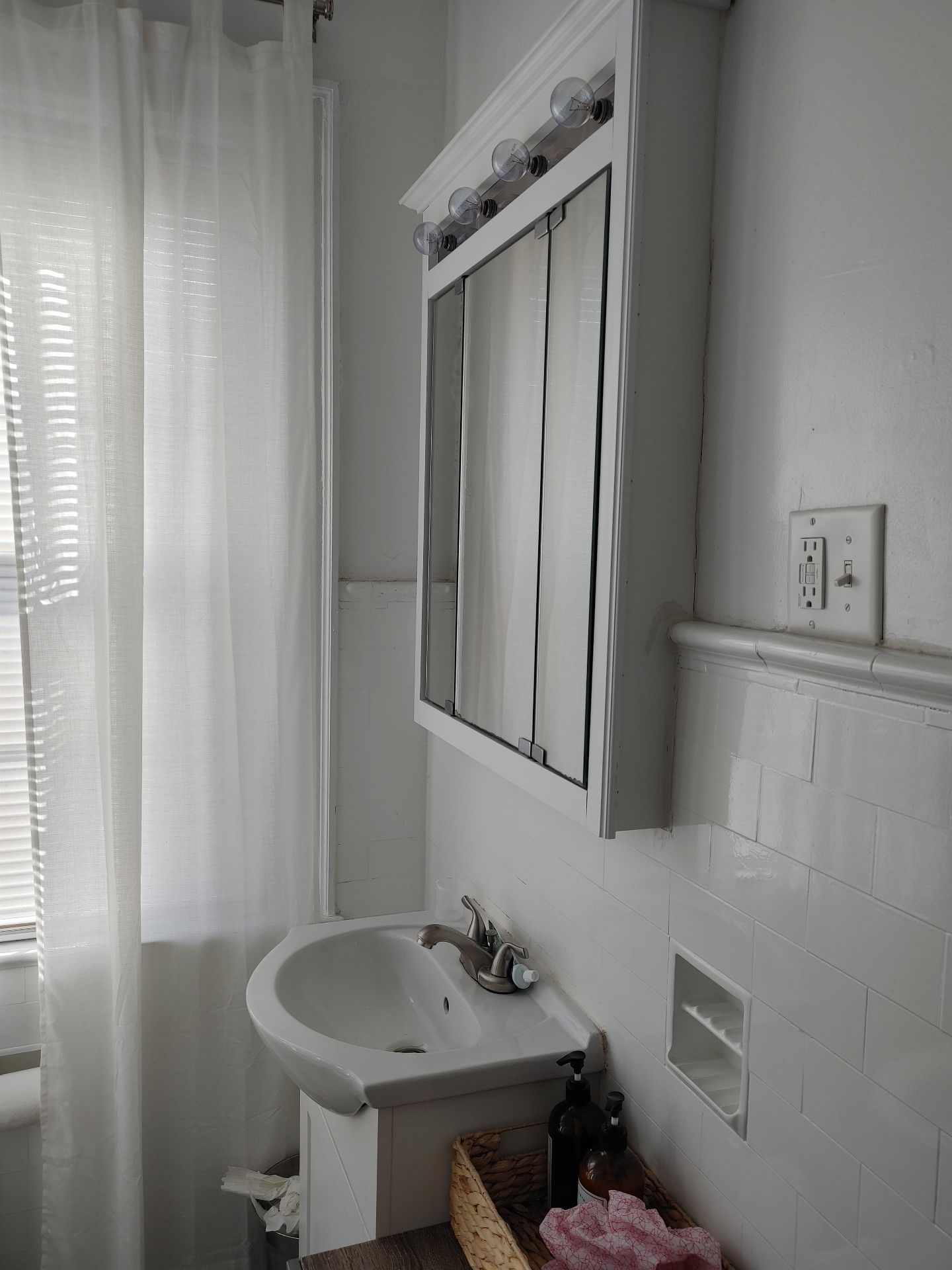 Unit G bathroom sink and mirrored medicine cabinet beside the shower curtain