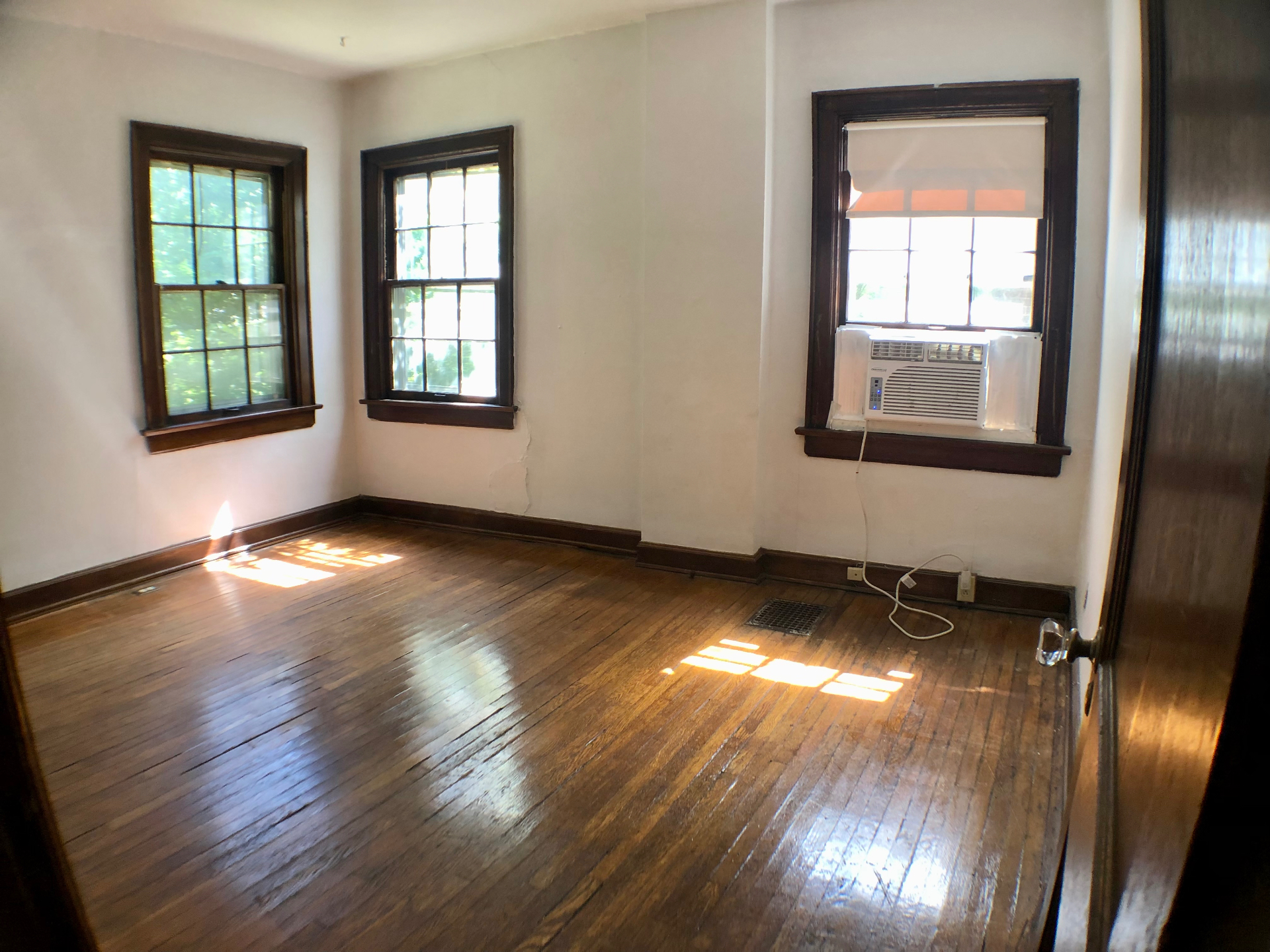 2044 Iuka Ave. A bright bedroom with three wood-trim windows, hardwood floors, and window AC