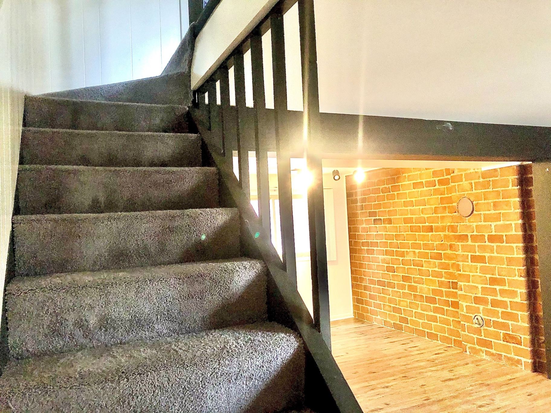 2011 Summit St. Unit C carpeted staircase with black railing and exposed red brick accent wall
