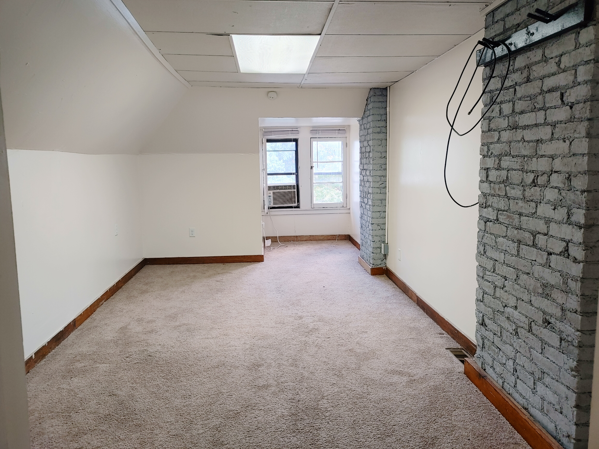 89 E Woodruff Ave. Unit C living area with window AC, exposed brick, and plush neutral carpet