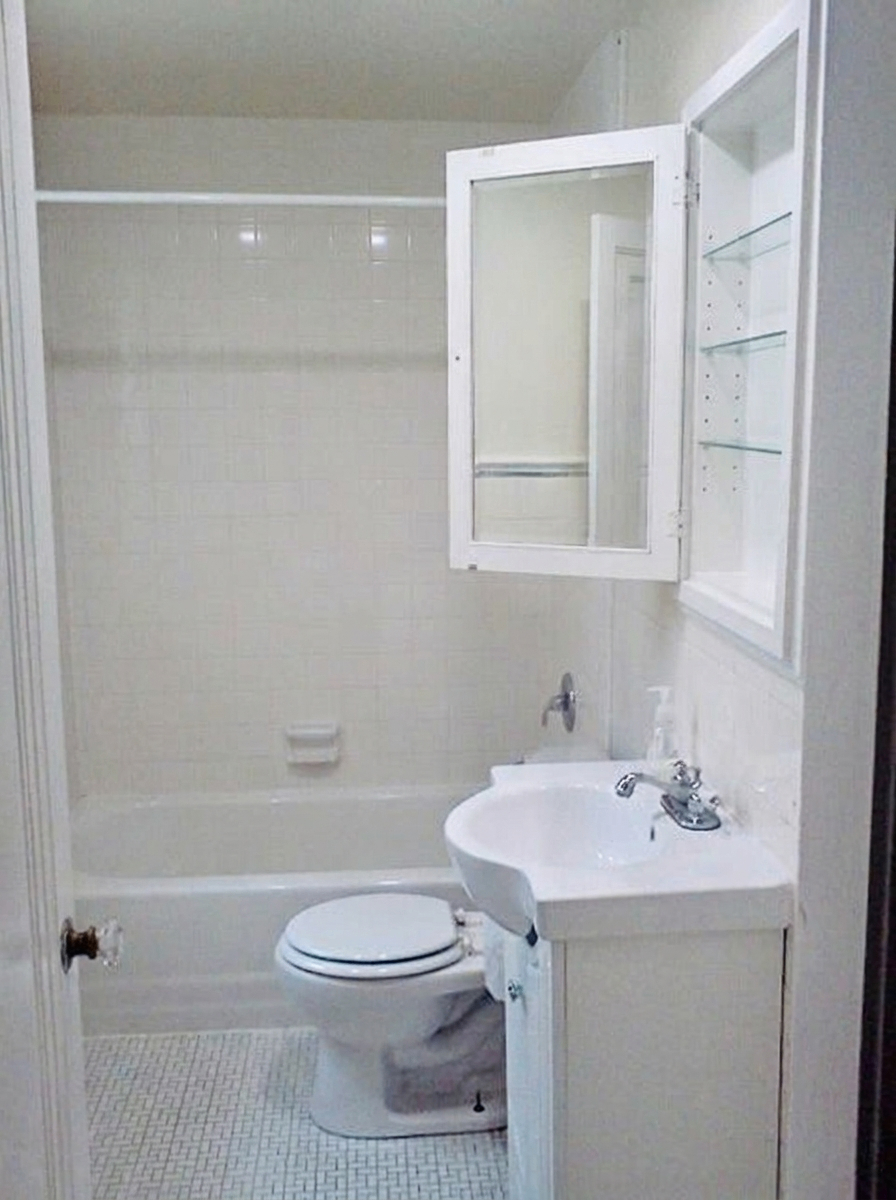 Unit D white tiled bathroom with tub, pedestal sink, and medicine cabinet