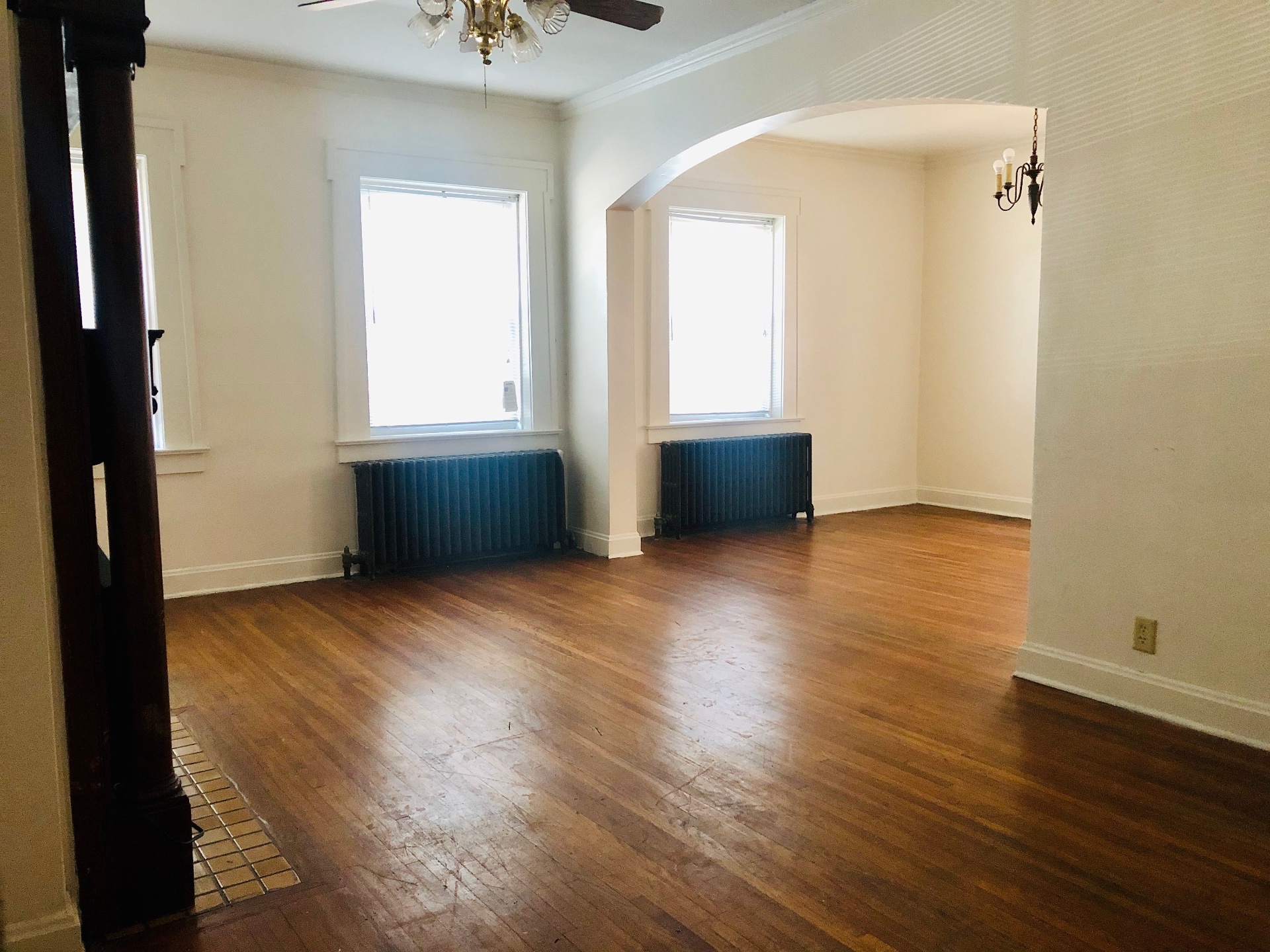 Unit G wide living and dining room with arched opening, hardwood floors, and twin radiators
