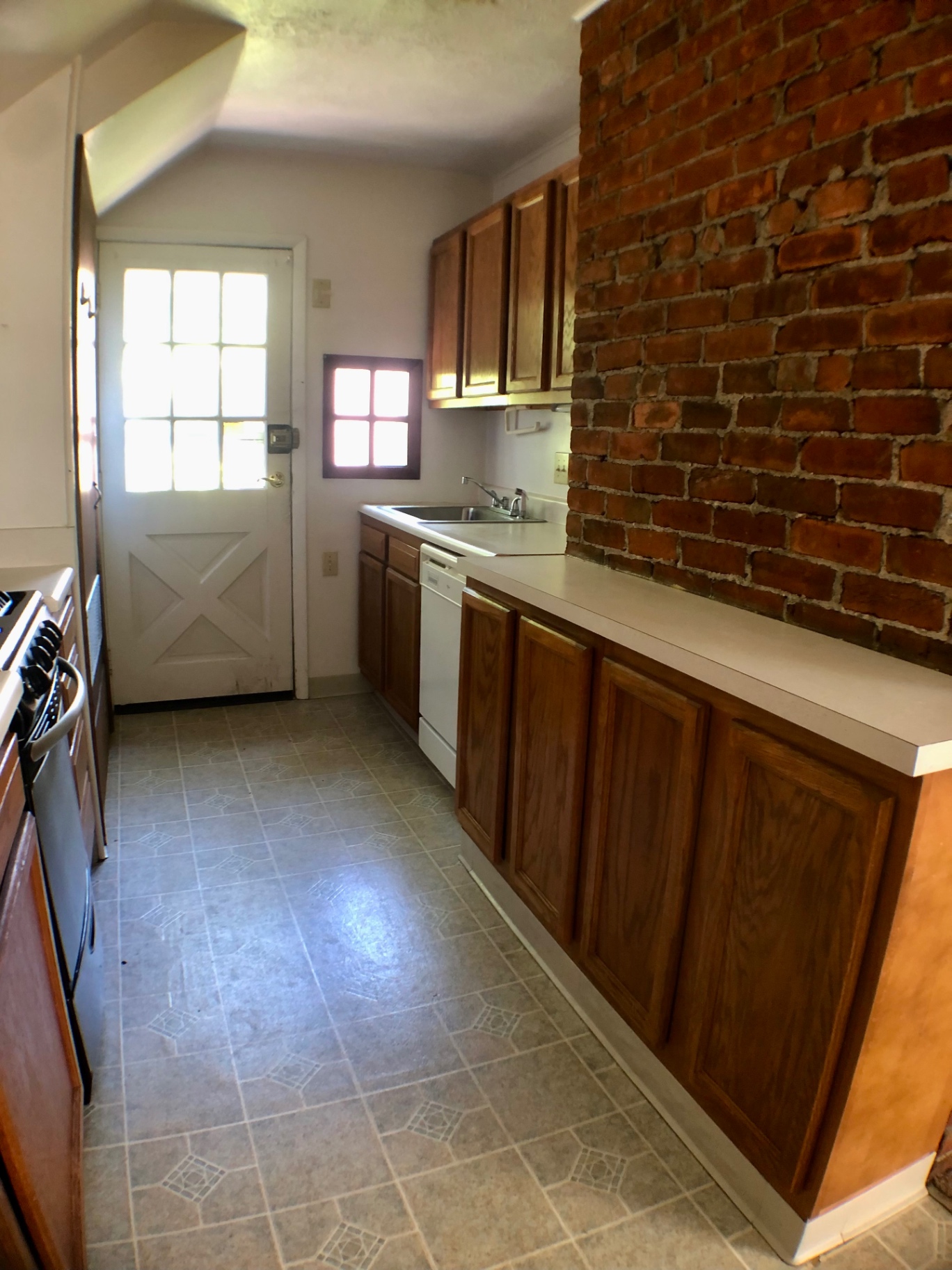 Galley kitchen with dishwasher, maple cabinets, and exposed brick chimney