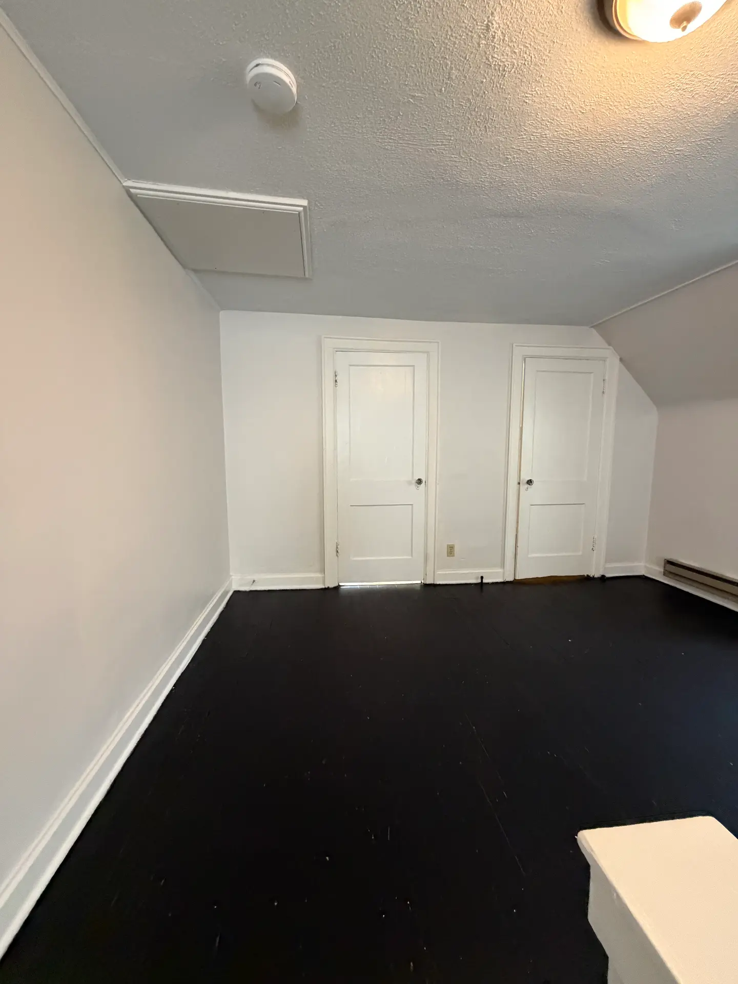 2048 Iuka Ave. D upstairs bedroom with two paneled closet doors, baseboard heat, and painted black hardwood floors