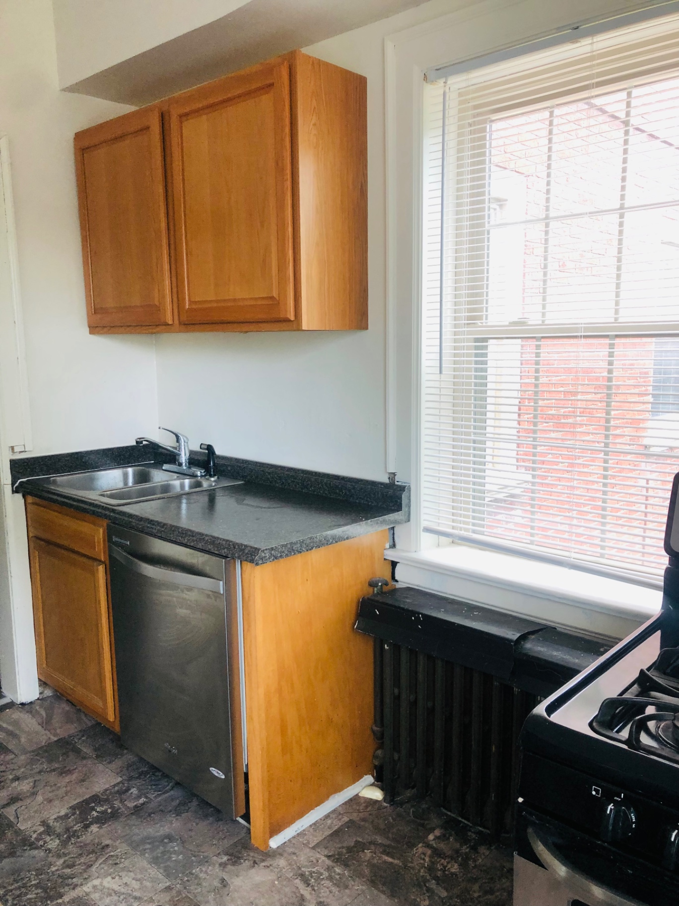 Unit F kitchen with stainless steel dishwasher, wood cabinets, and window