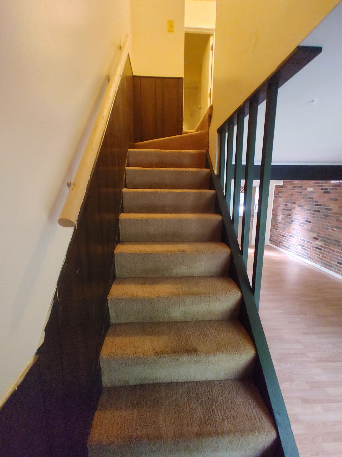 2018 Iuka Ave. carpeted staircase with wood handrail and exposed brick accent wall