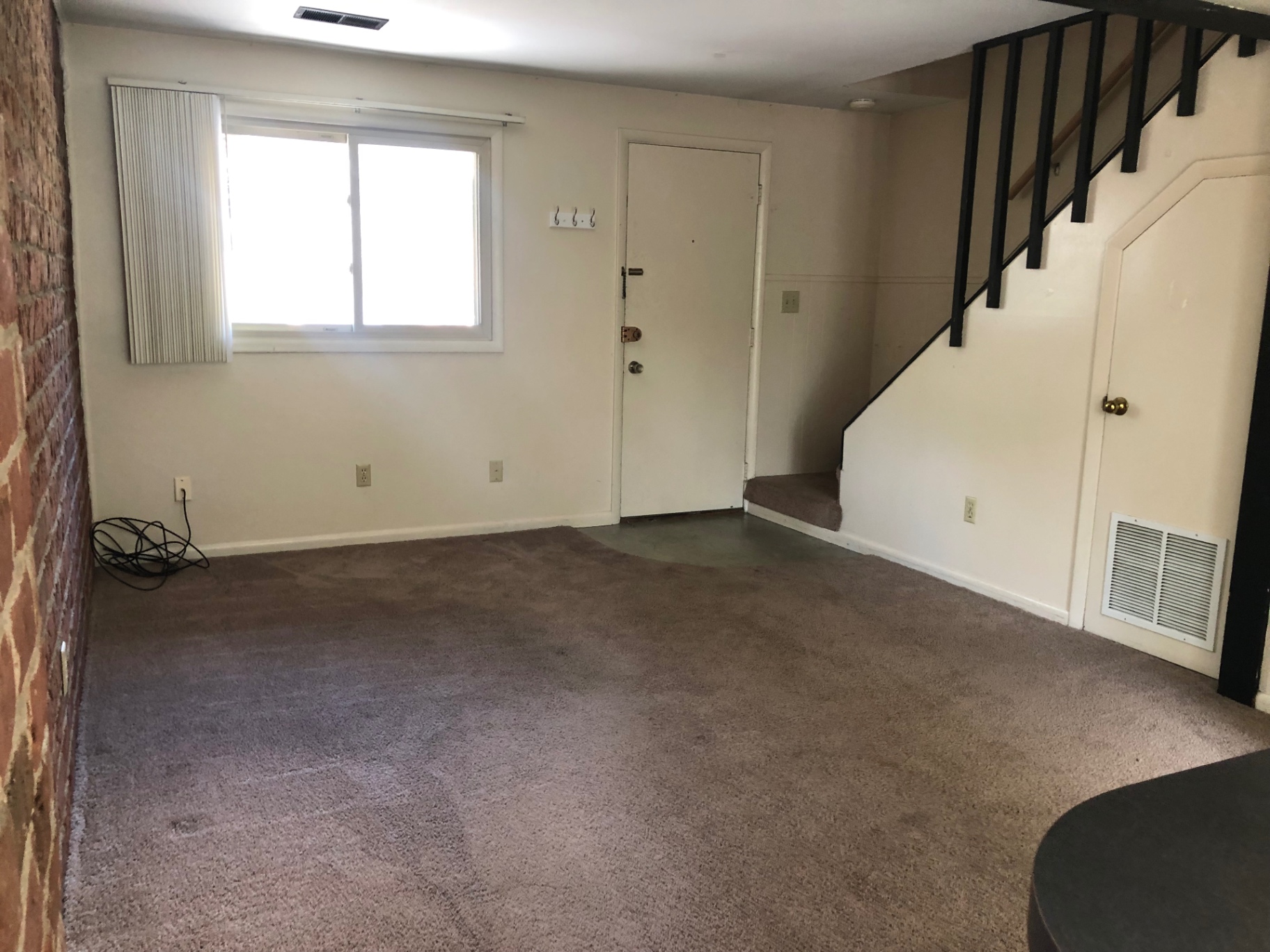 2011 Summit St. Unit F open living room with wood-look plank floors, exposed brick, and staircase with black railing
