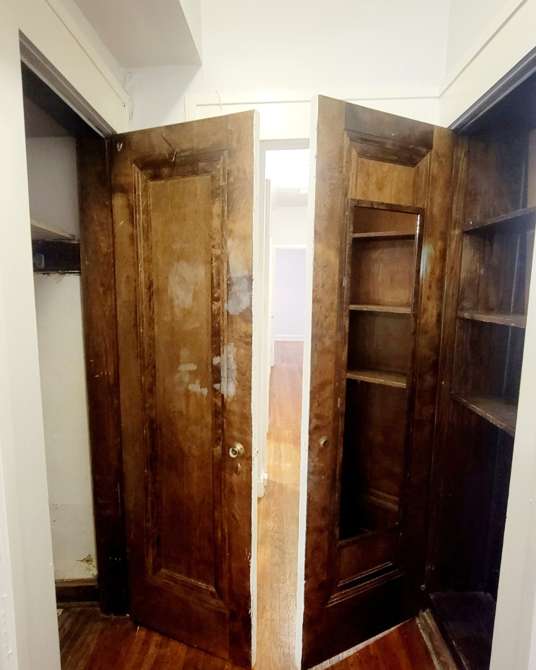 Unit A hallway closet area with original wood doors and built-in shelving