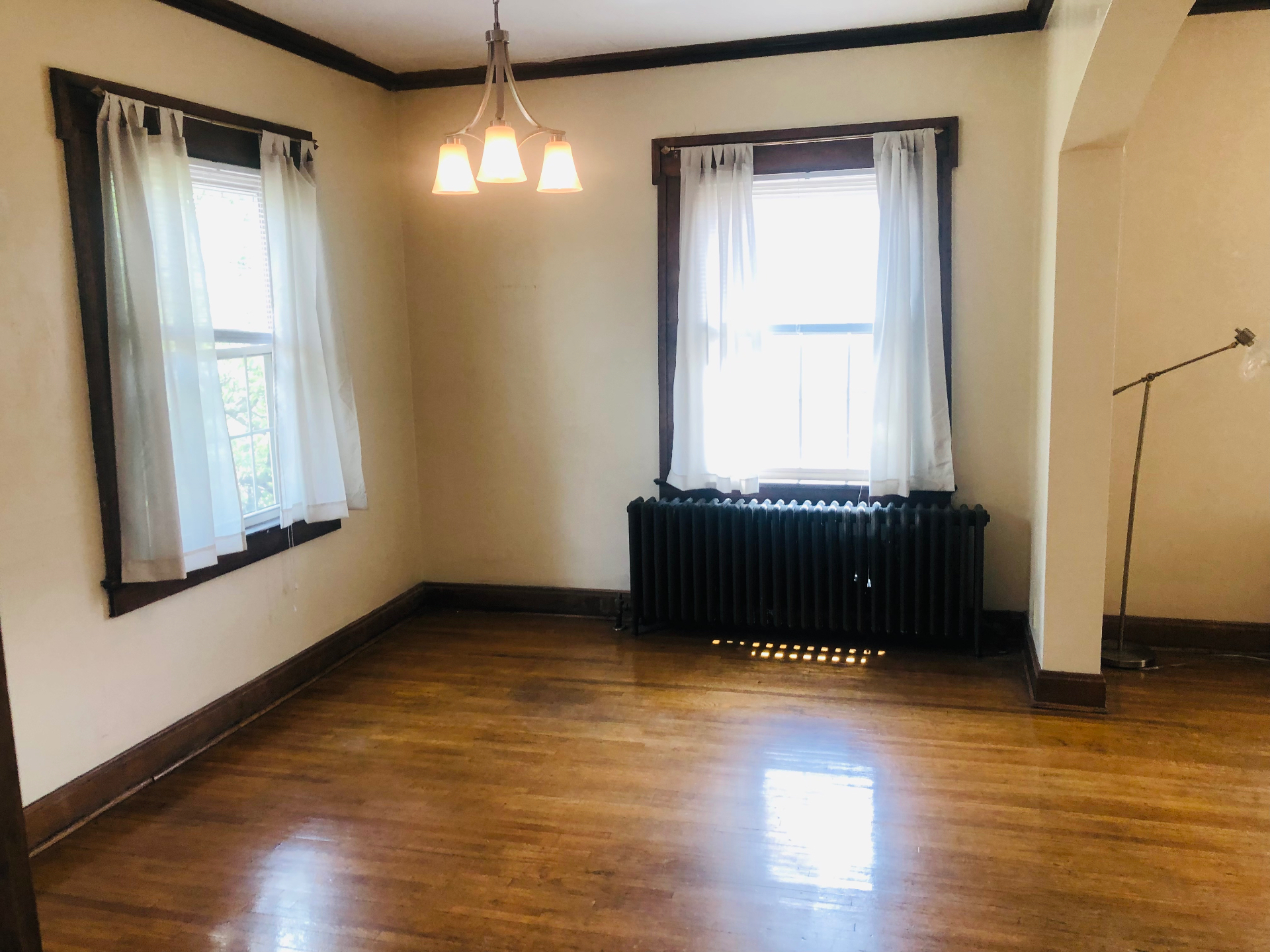 Unit K dining area with large windows, curtains, cast iron radiator, and hardwood floors
