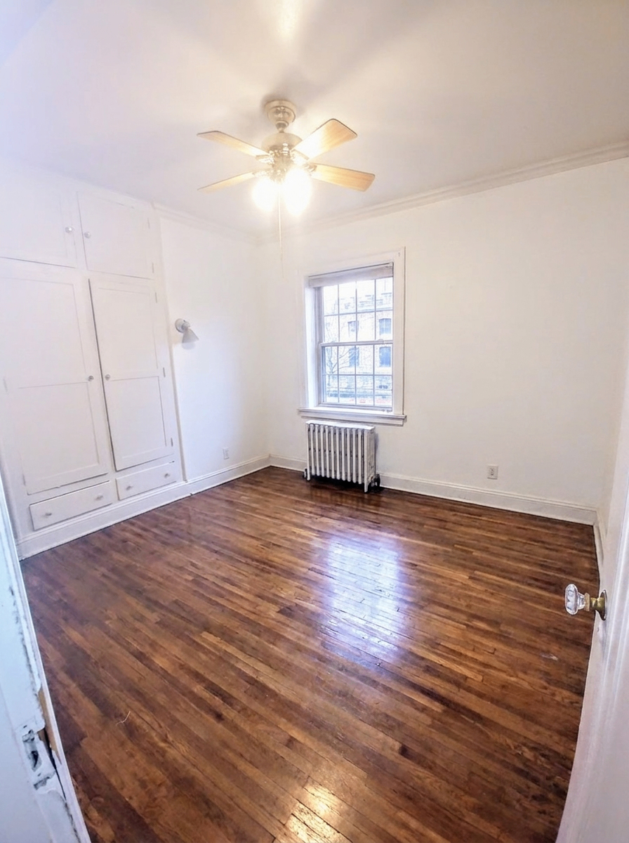Unit B bedroom with built-in white cabinets, ceiling fan, and large window