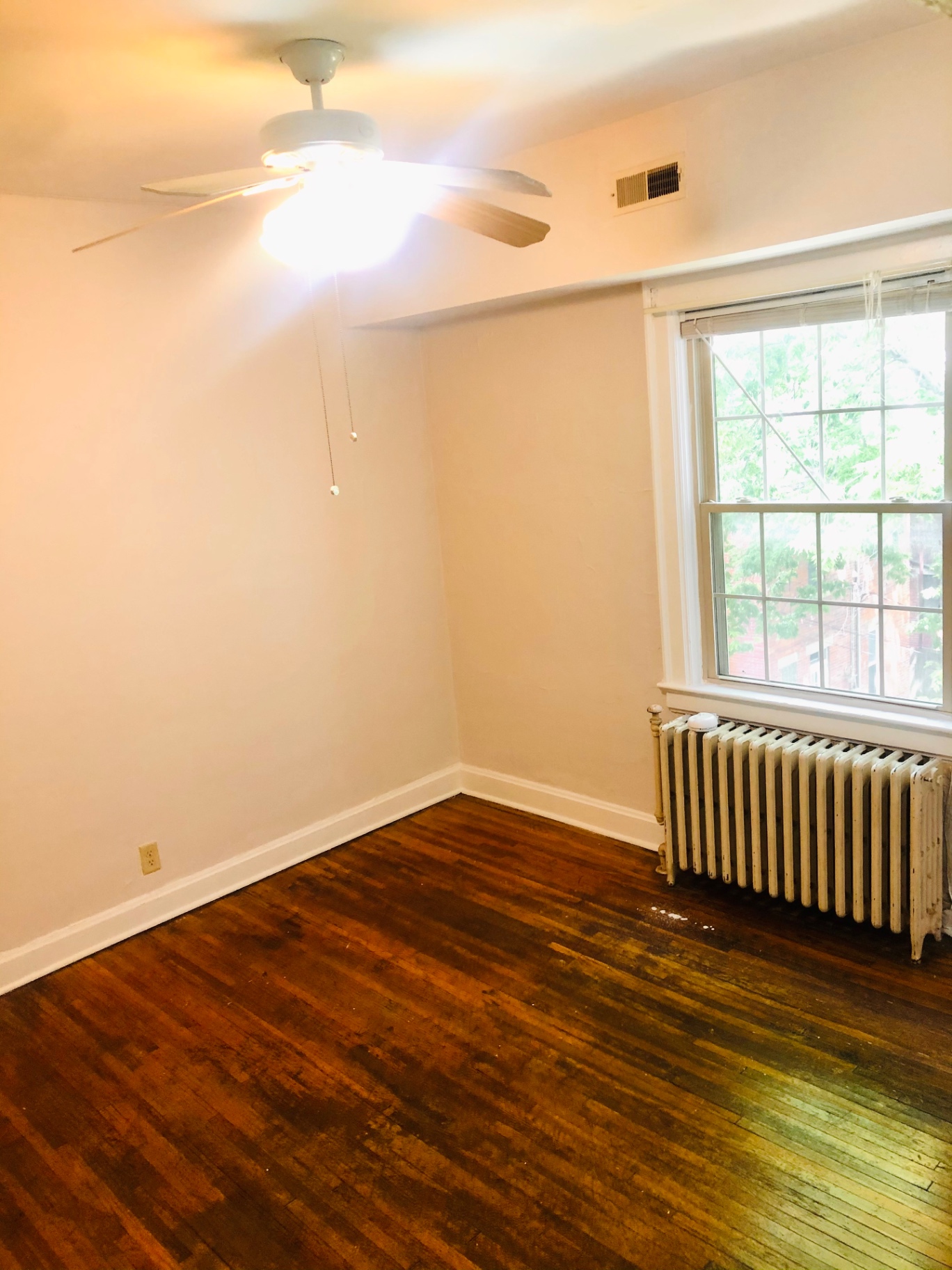 Unit L bedroom with hardwood floors, ceiling fan, and large window