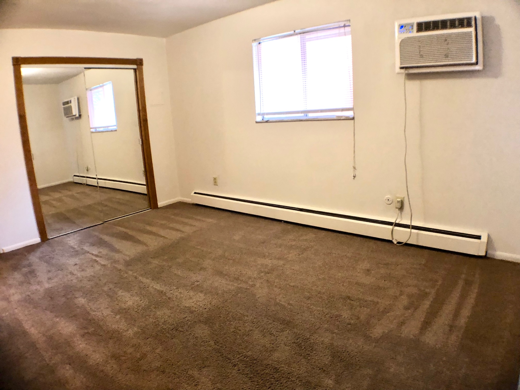 1827 N 4th St. Unit 4 carpeted bedroom with mirrored closet doors, window AC, and baseboard heat