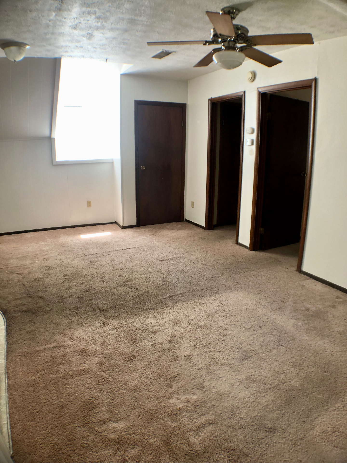 Open carpeted living room with vaulted ceiling, ceiling fan, and dark wood trim