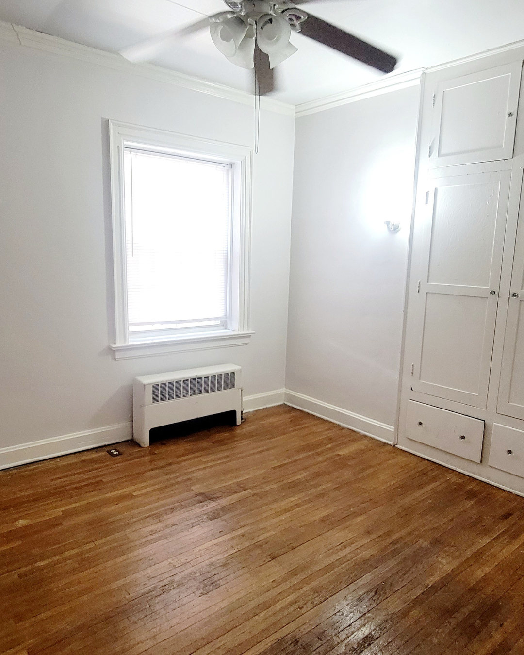 Unit A bedroom with hardwood floors, built-in cabinets, and ceiling fan