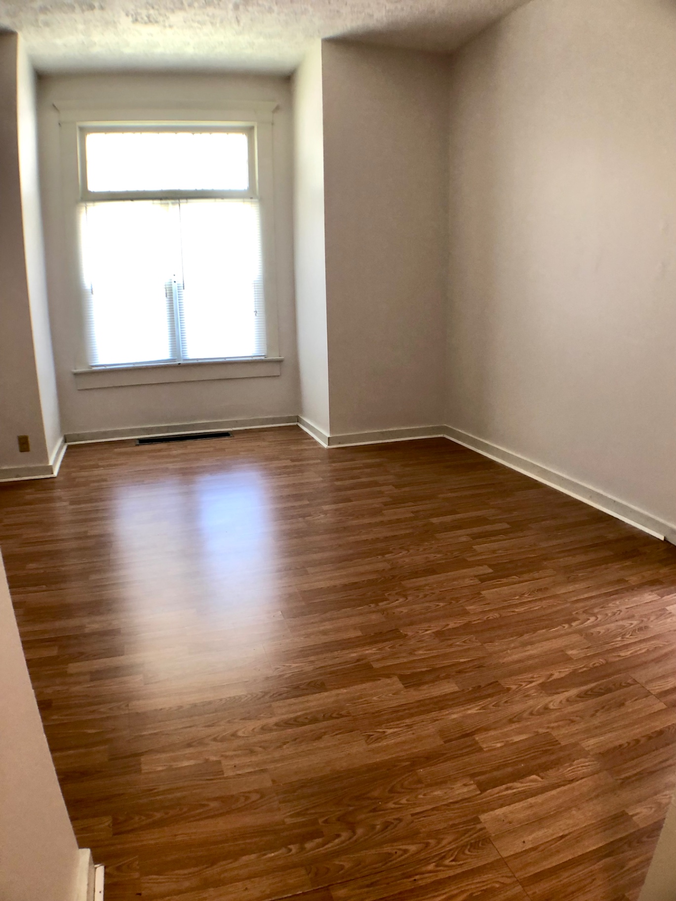 Unit A room with hardwood floors and tall window with blinds