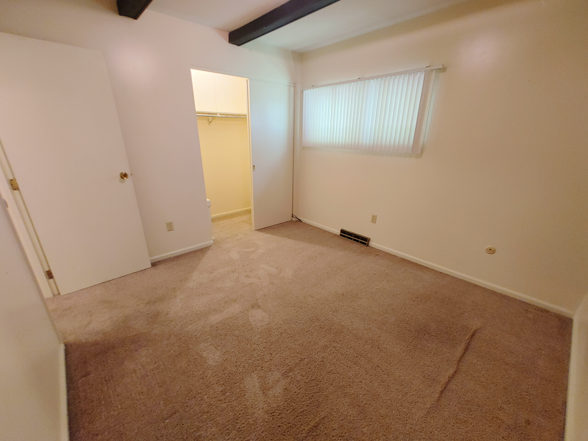 2016 Iuka Ave. bedroom with large window, vertical blinds, walk-in closet, and exposed ceiling beam