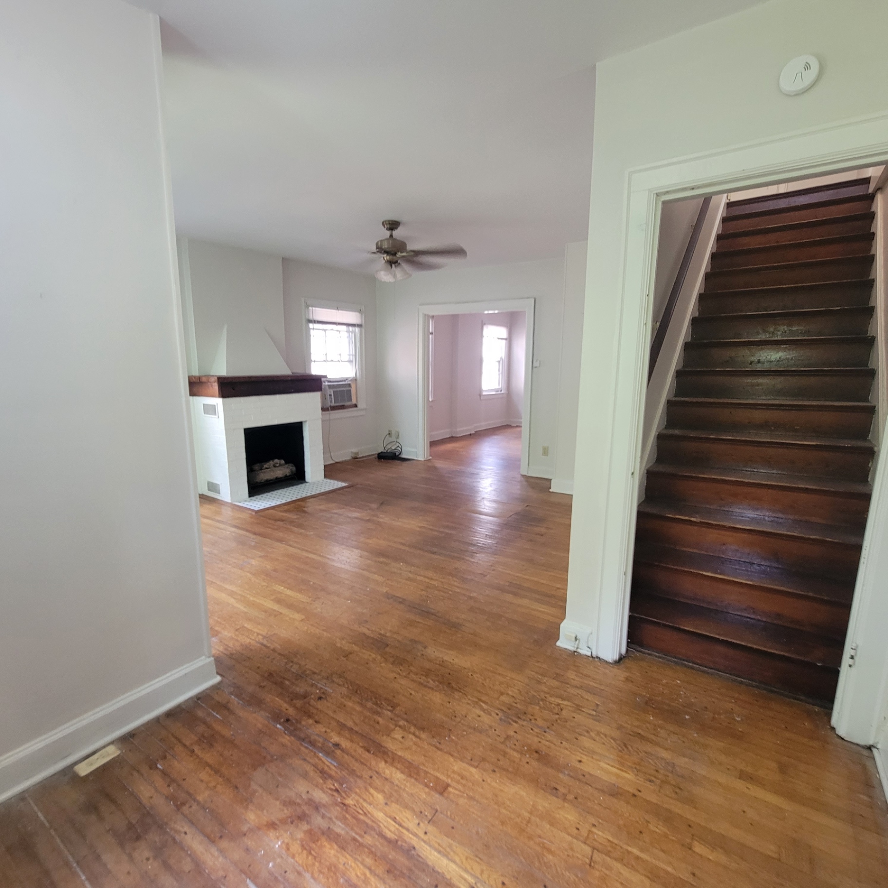 2048 Iuka Ave. C main-floor living room with white brick fireplace, hardwood floors, and staircase to upstairs bedroom