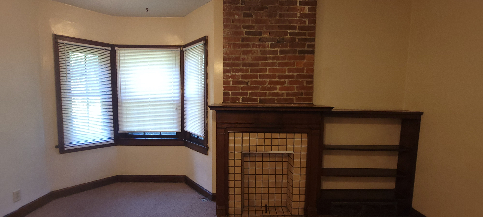 2054 Iuka Ave. C detail of tile fireplace with original wood mantel, exposed brick, and built-in bookshelf
