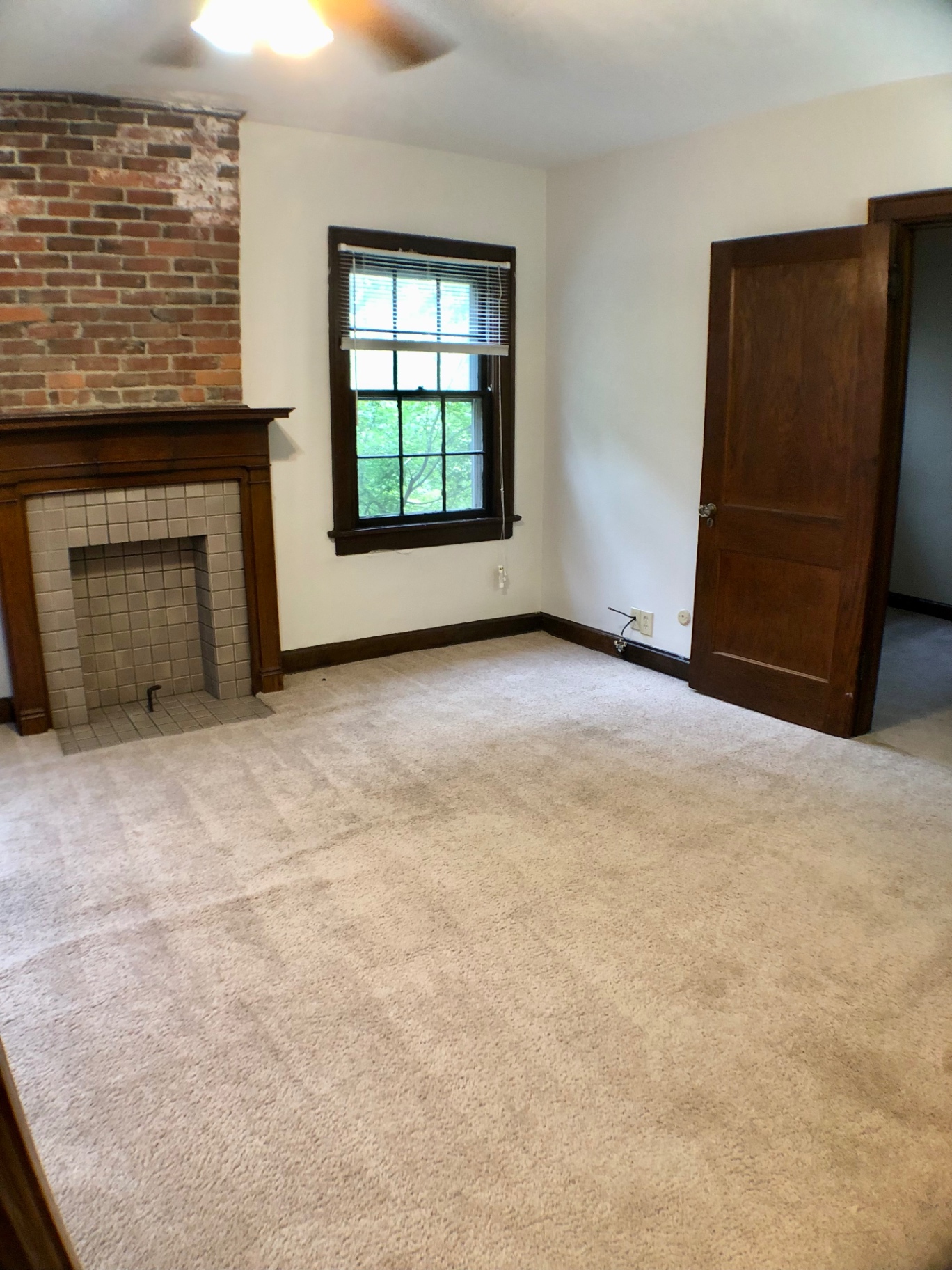 2054 Iuka Ave. D living room angle showing tile fireplace, ceiling fan, exposed brick, and original wood doors