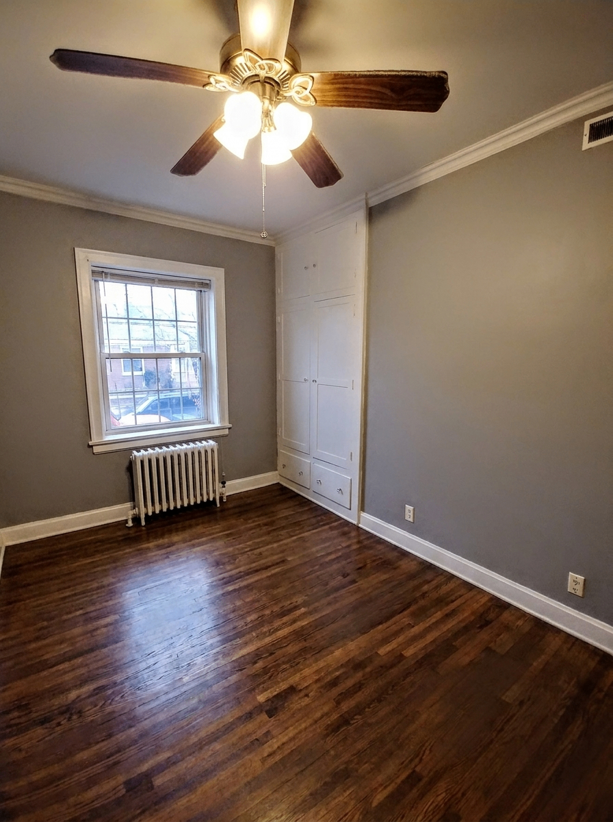 Unit B bedroom with gray walls, built-in cabinets, ceiling fan, and radiator