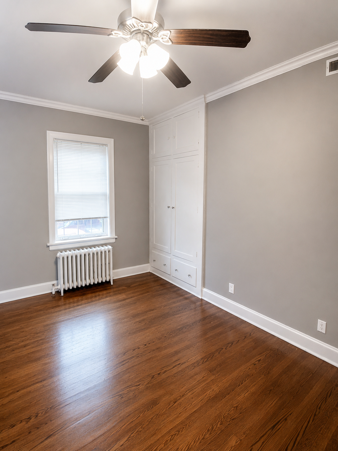 Unit B bedroom with hardwood floors, built-in white cabinets, ceiling fan, and window