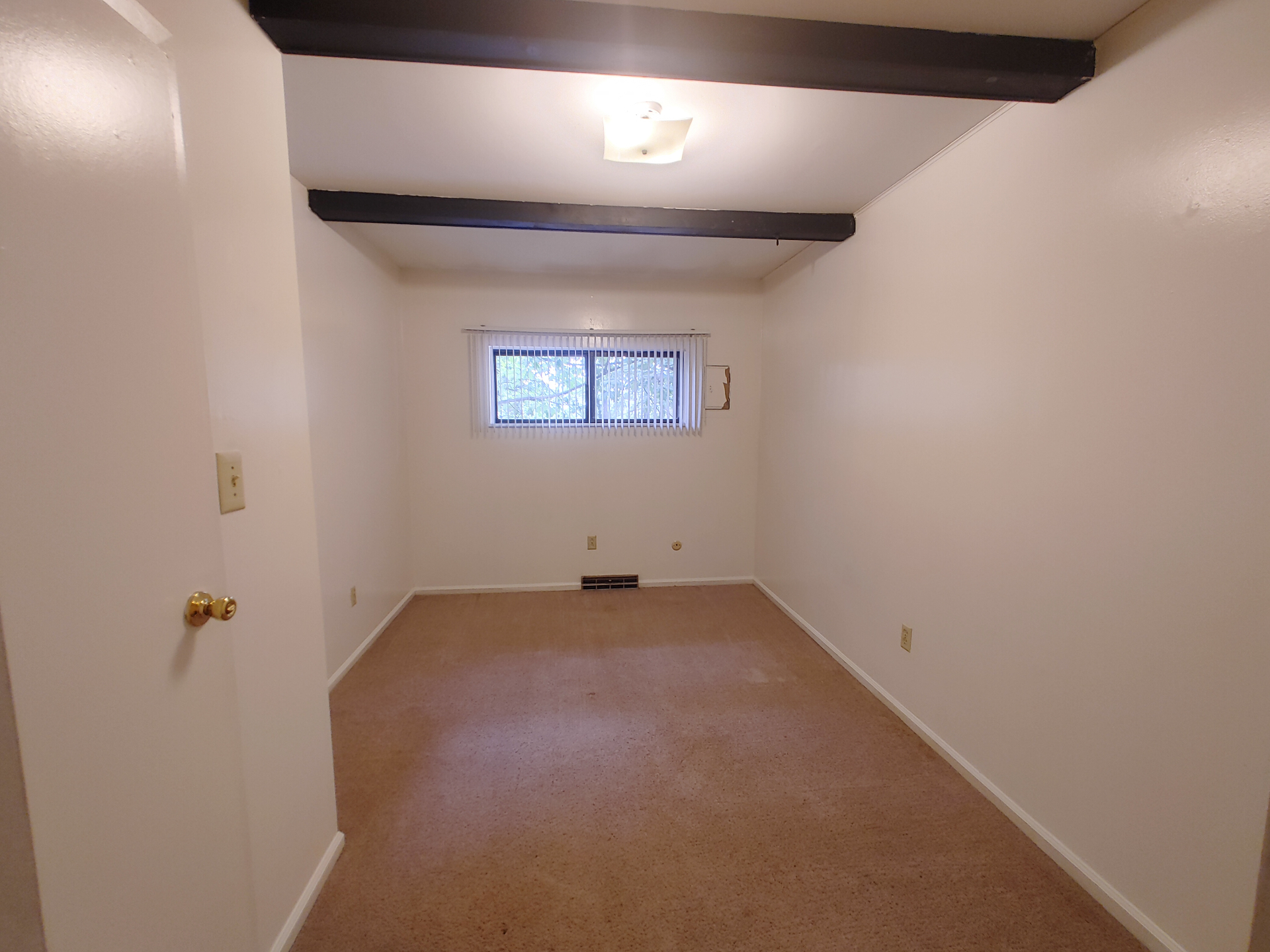 2020 Iuka Ave. bedroom with dark ceiling beams, fresh carpet, and a window overlooking trees