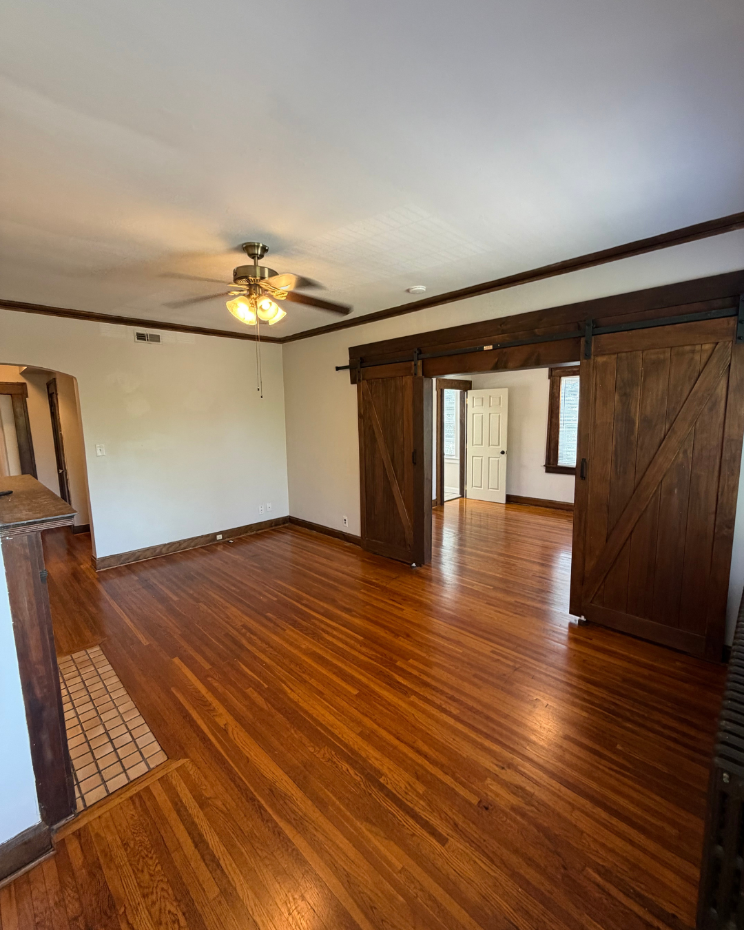 Open living area with barn doors, ceiling fan, and hardwood floors
