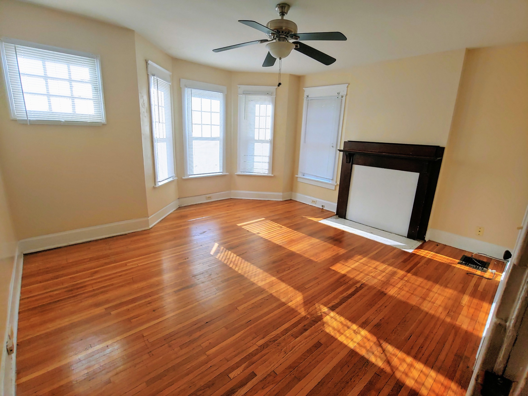 1818 Summit St. sunlit bay-window living room with dark wood mantel and refinished hardwood floors