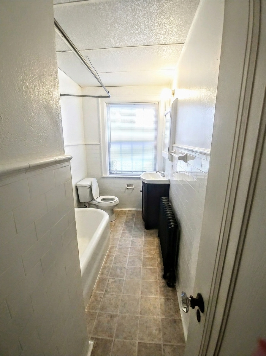 Unit I bathroom with tub, vanity, radiator, and tiled floor
