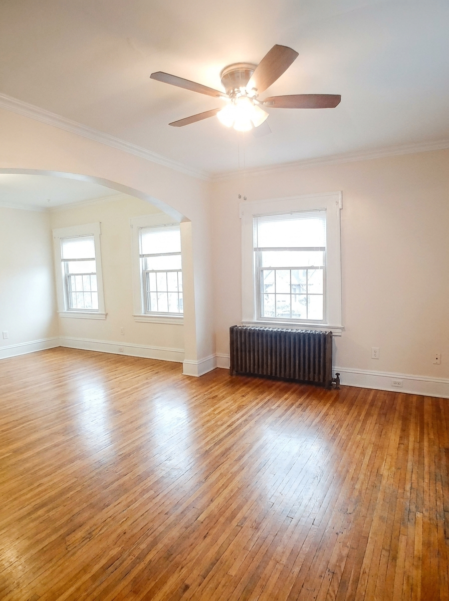 Unit C living area with large windows, ceiling fan, and radiator