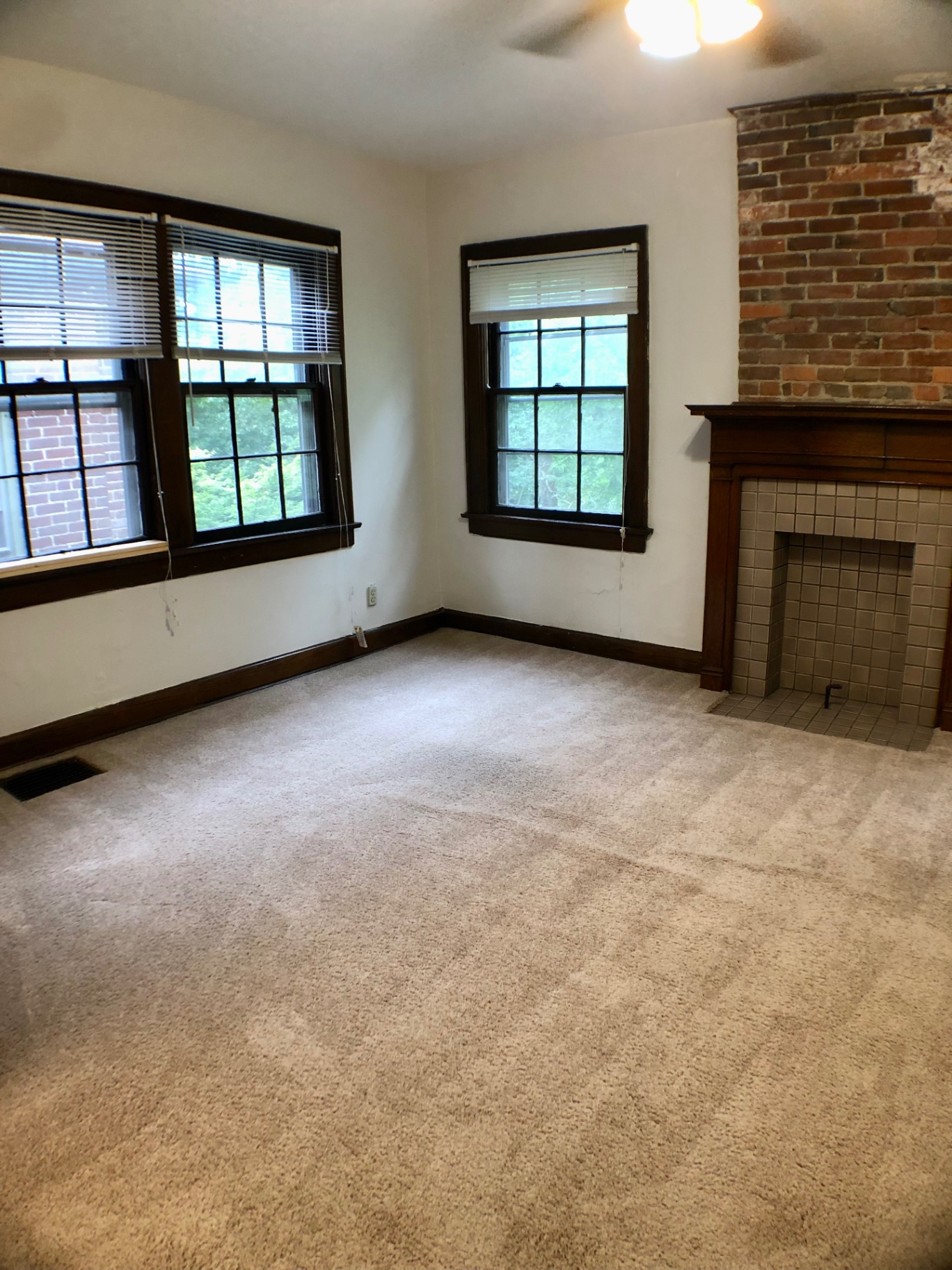 2054 Iuka Ave. D living area with tile fireplace, exposed brick, three windows, and ceiling fan