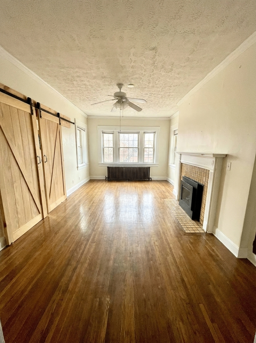 Unit H spacious living room with hardwood floors, barn doors, bay window, and tiled fireplace