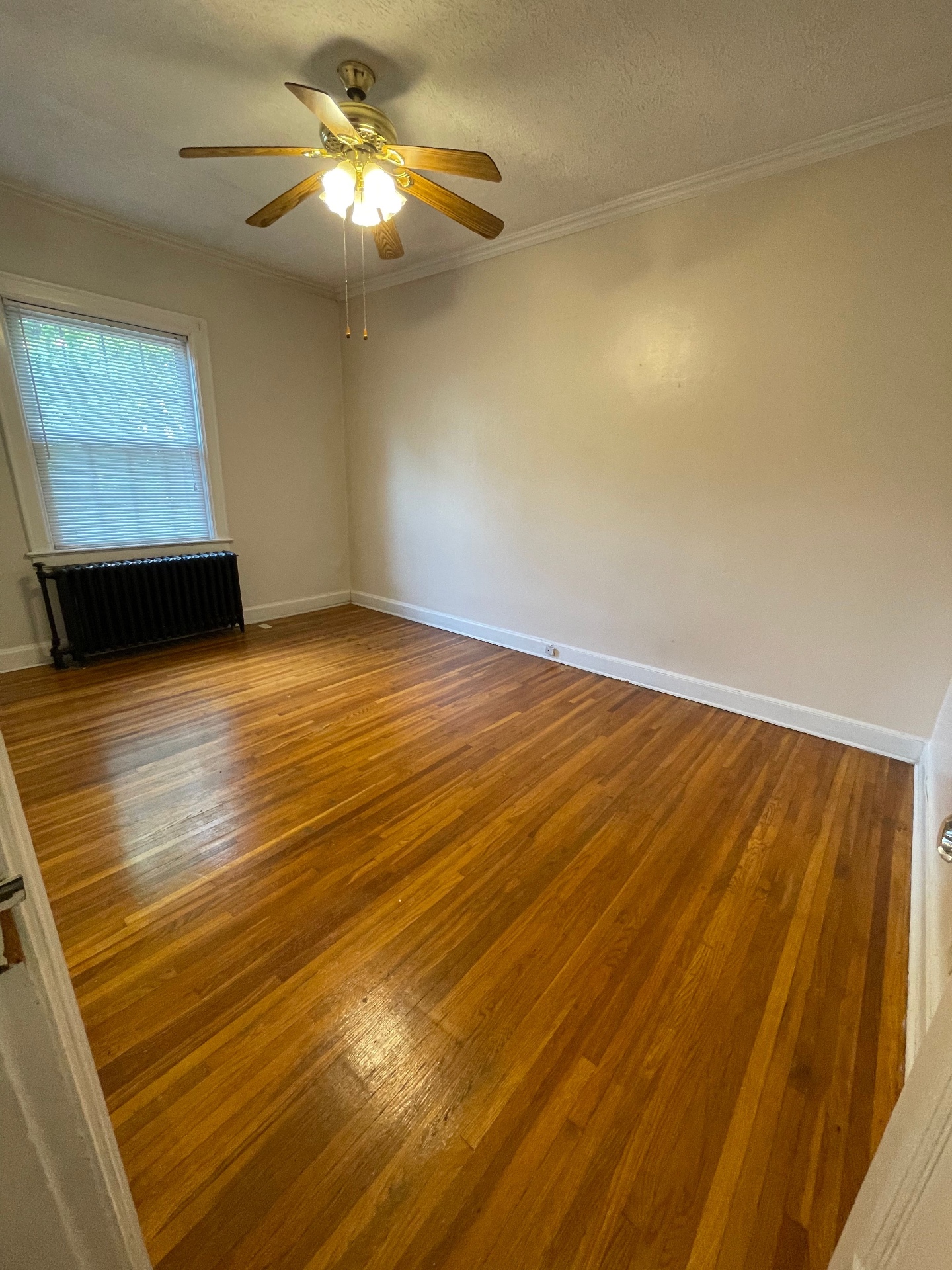 Unit E bedroom with radiator, ceiling fan, and hardwood floors