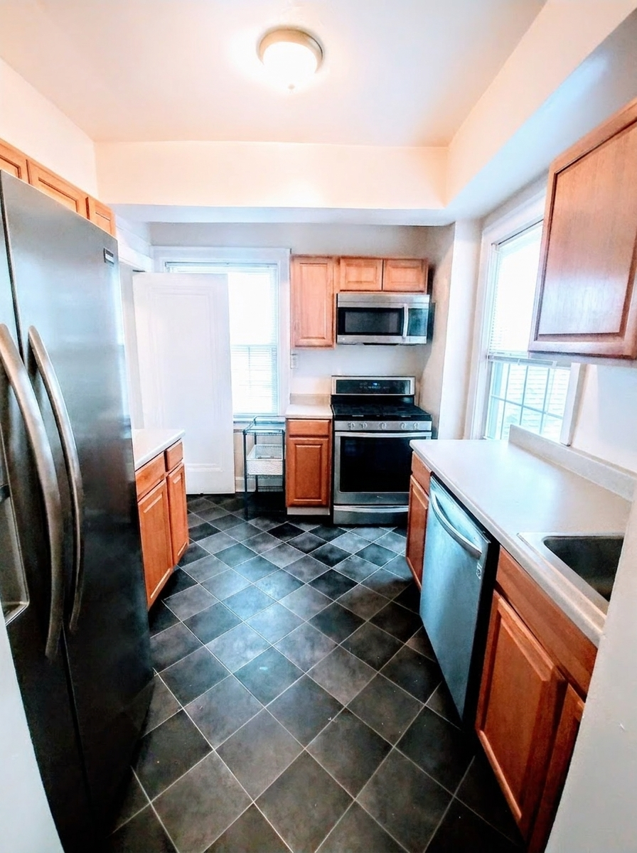 Unit I galley kitchen with stainless steel appliances, dishwasher, and dark tile floor