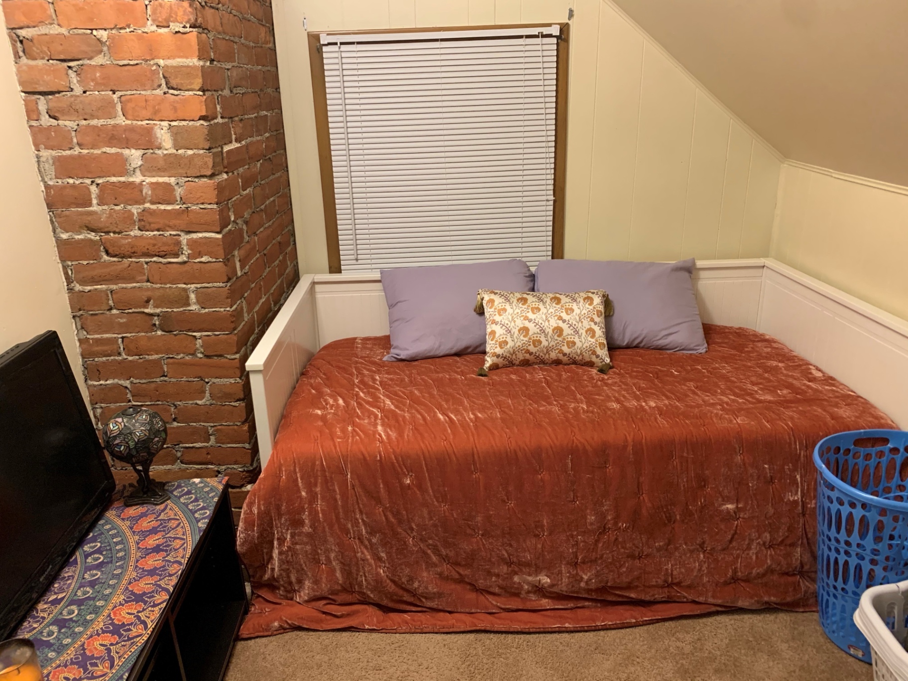 Daybed with orange coverlet against exposed brick wall in flex room