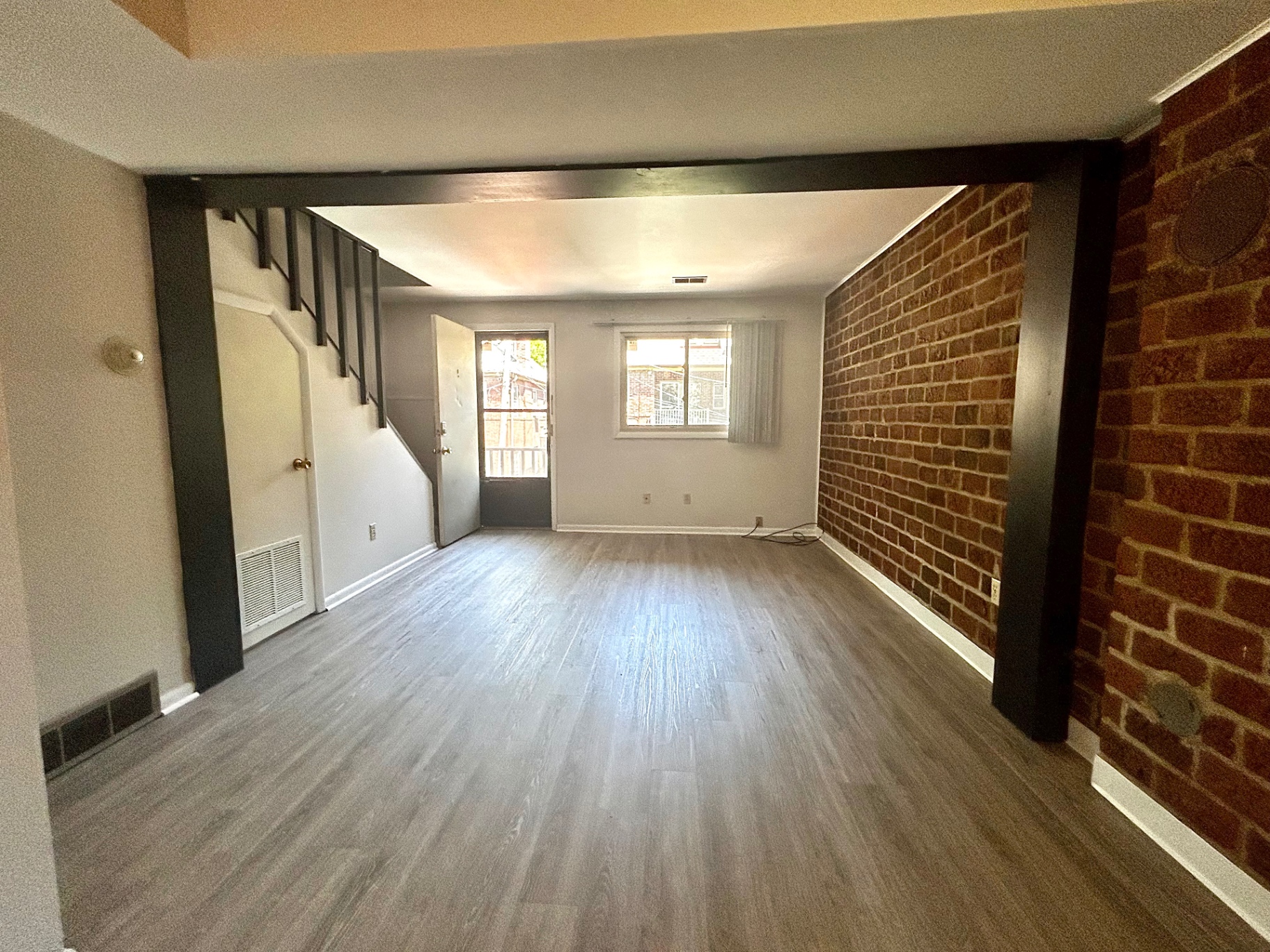 2011 Summit St. Unit E open living room with exposed red brick accent wall, plank floors, and staircase