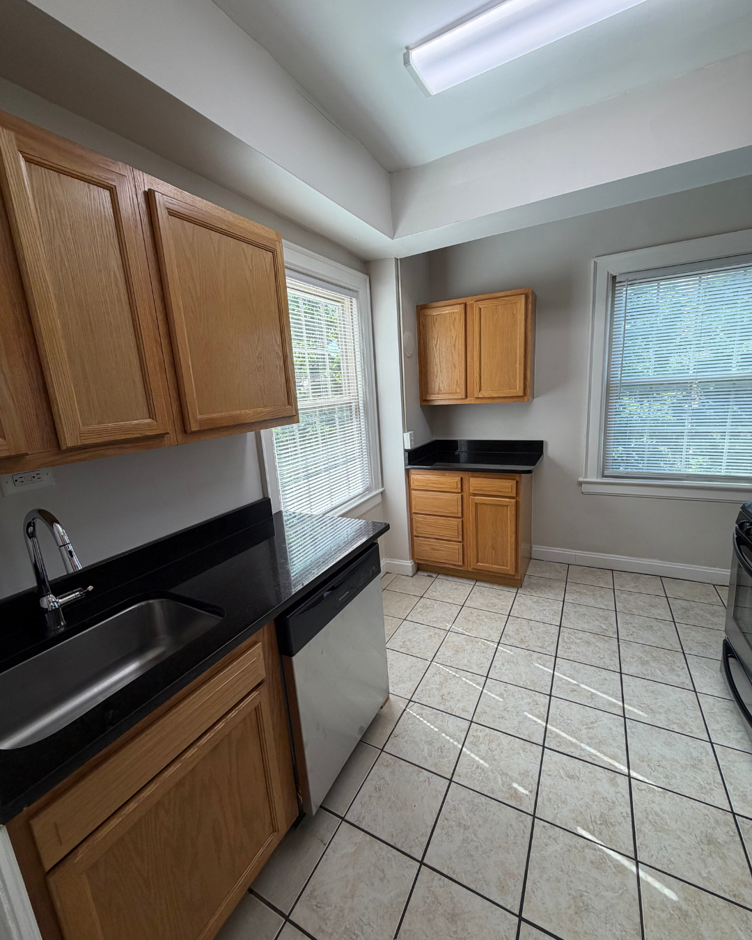 Kitchen with oak cabinetry, granite counters, dishwasher, and dual windows