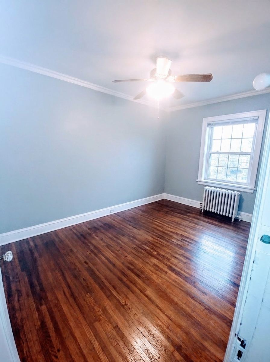 Unit B bedroom with light blue walls, ceiling fan, and radiator under window