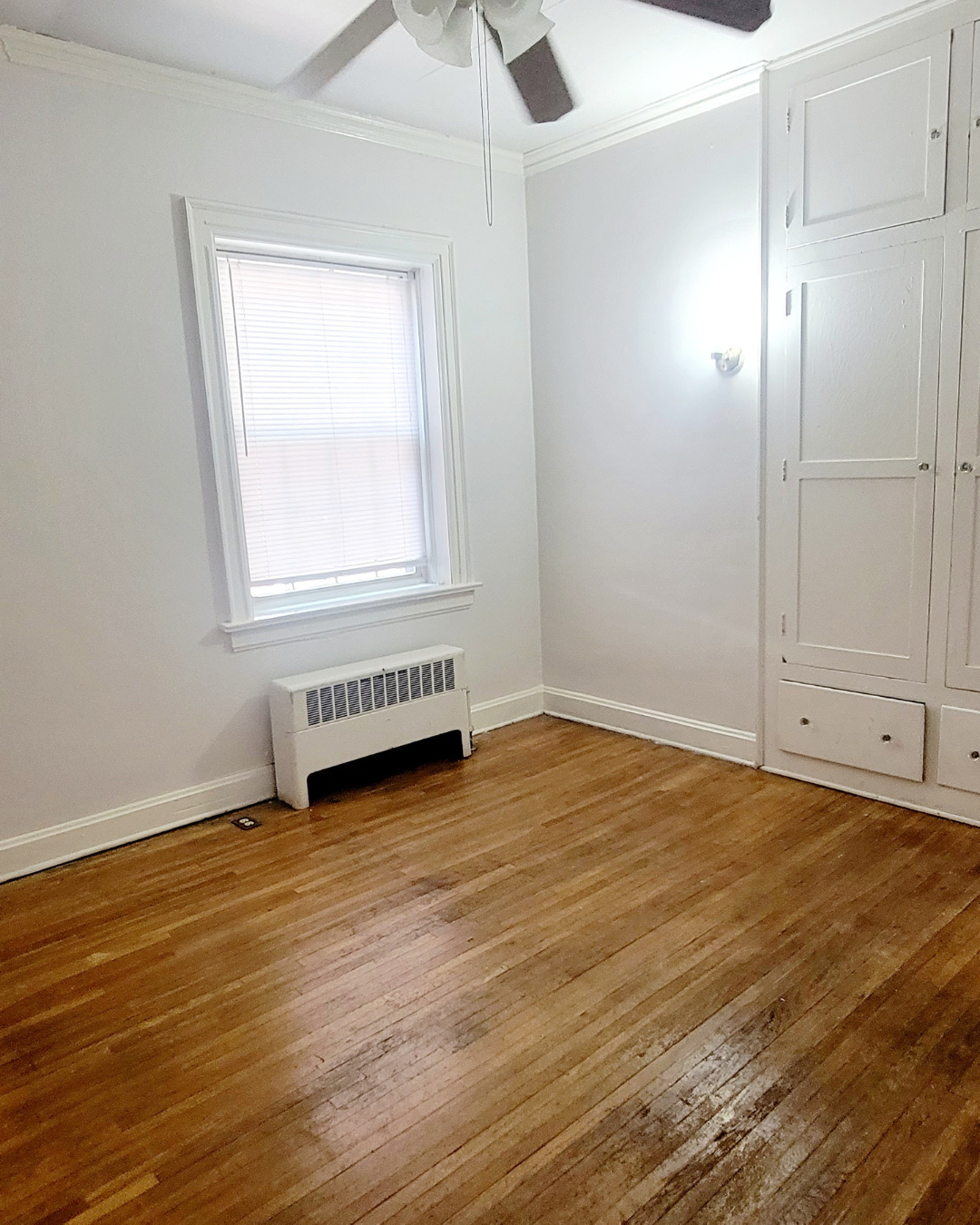 Unit A bedroom with hardwood floors, built-in storage, and window radiator