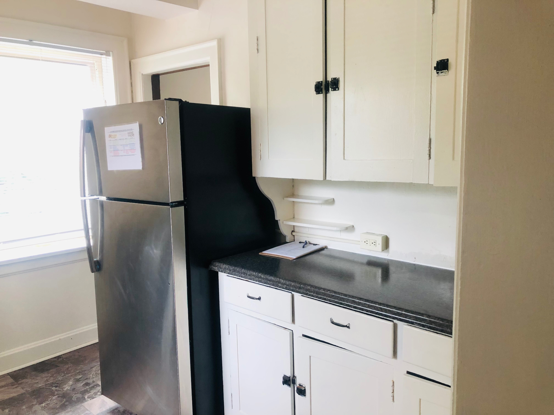 Unit F kitchen with stainless steel refrigerator, white cabinets, and granite countertops